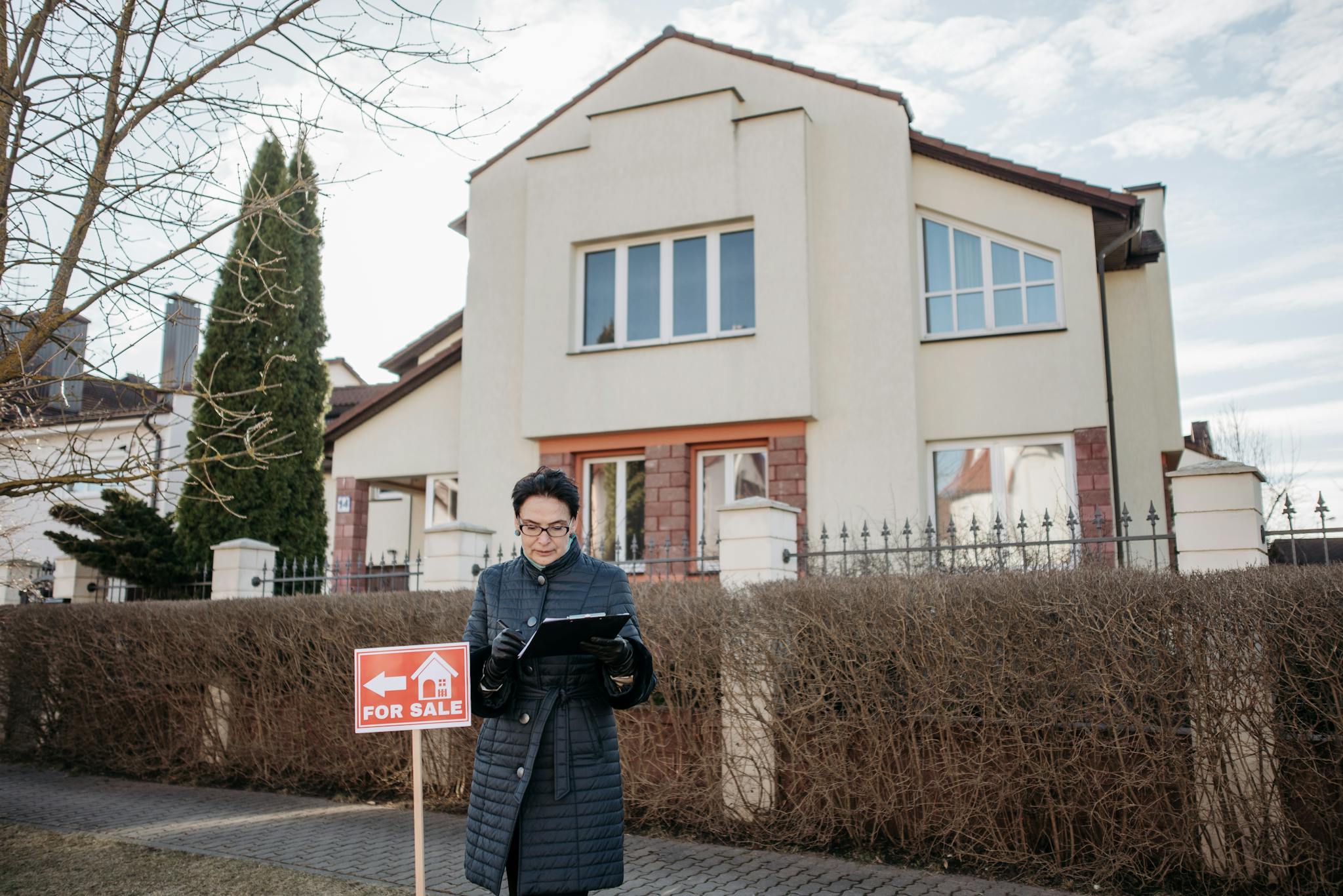 A real estate agent standing outside a house with a 'For Sale' sign, ready for viewing.